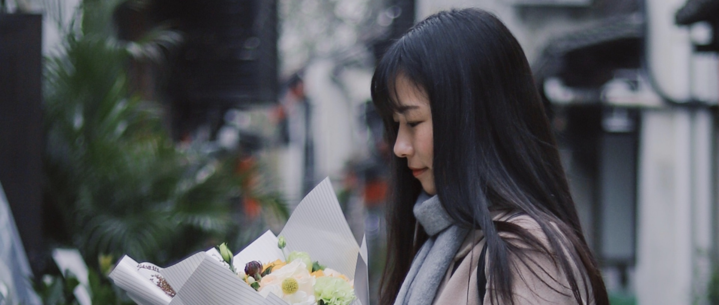 Woman on a London street holding a hand-tied bouquet of white and yellow flowers